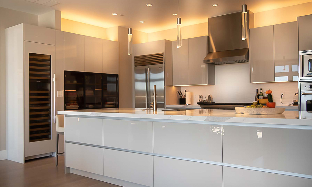 A contemporary L-shaped kitchen featuring glossy white lacquer cabinets and a central countertop island. The high-gloss finish reflects light beautifully, creating a bright and airy atmosphere. The central island adds both functionality and a stylish focal point, perfectly complementing the modern design of the kitchen.