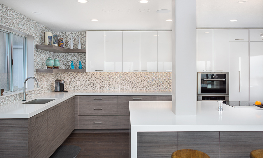 A close-up of an L-shaped kitchen featuring light wood veneer base cabinets and glossy white upper cabinets. The kitchen is complemented by a white countertop on the central island, enhancing the clean and modern aesthetic. The light wood finish adds warmth, while the bright white surfaces create a sleek, airy atmosphere, showcasing a harmonious blend of natural and contemporary design elements.