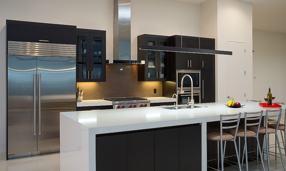 A linear kitchen featuring dark lacquered cabinets with a central island. The sleek, glossy finish of the dark cabinetry contrasts with the modern design of the island, creating a stylish and functional space. The kitchen's minimalist layout and contemporary elements add to its clean, sophisticated look.