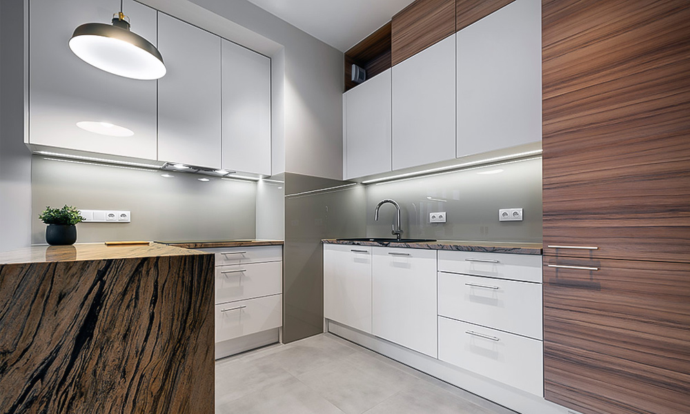A close-up view of a modern one-wall kitchen with white lacquered cabinetry and a white countertop central island. The design emphasizes the smooth, glossy finish of the white cabinets and island, offering a bright, clean, and contemporary aesthetic.