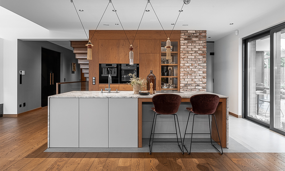 A modern kitchen with wood veneer cabinets, bringing a warm and natural feel to the space. The focal point is a light gray marble island countertop, adding a touch of elegance and subtle sophistication. The overall design is sleek and contemporary, with soft lighting enhancing the clean, stylish aesthetic.